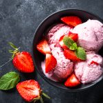 Strawberry ice cream with fresh berries in a bowl on black. Top view with copy space.