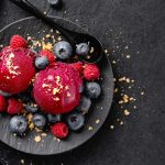 Tasty appetizing summer refreshing ice cream scoops with wild berries served on dark plate on dark background.